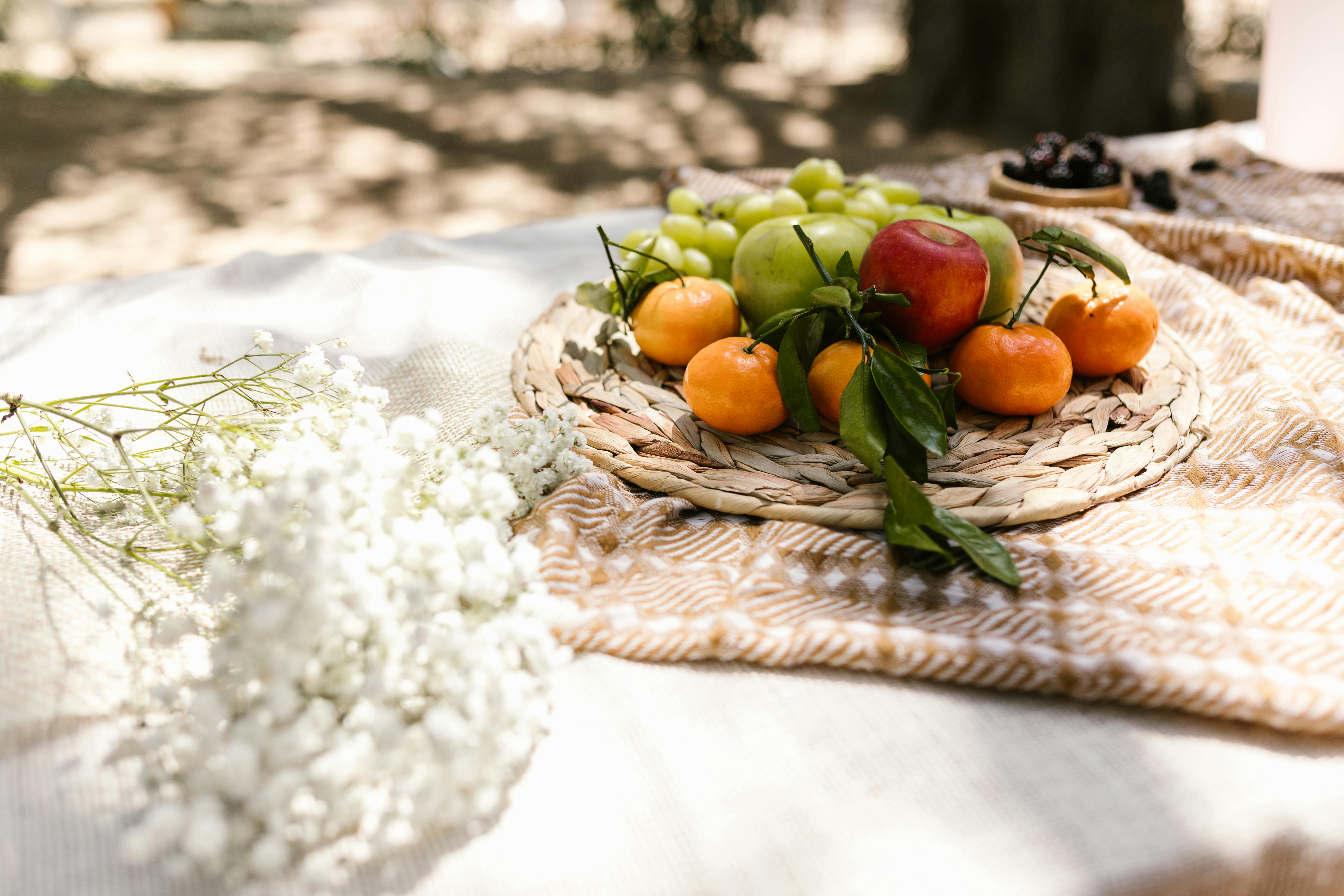 A colorful picnic setup featuring apples, grapes, and white flowers on a blanket.