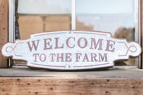 Free Rustic metal welcome sign reading 'Welcome to the Farm' on a wooden background, capturing a rural ambiance. Stock Photo