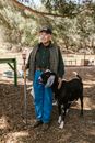 Elderly Man standing beside a Black Goat