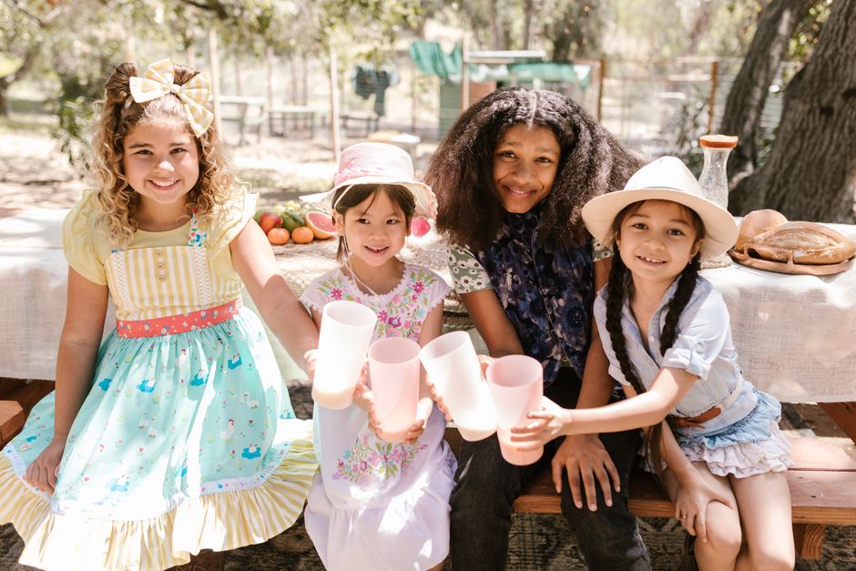 Four children smiling and holding cups at an outdoor picnic table.