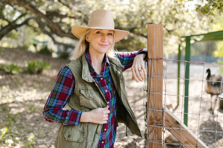 Blonde Woman Wearing Straw Hat Standing Beside The Fence 