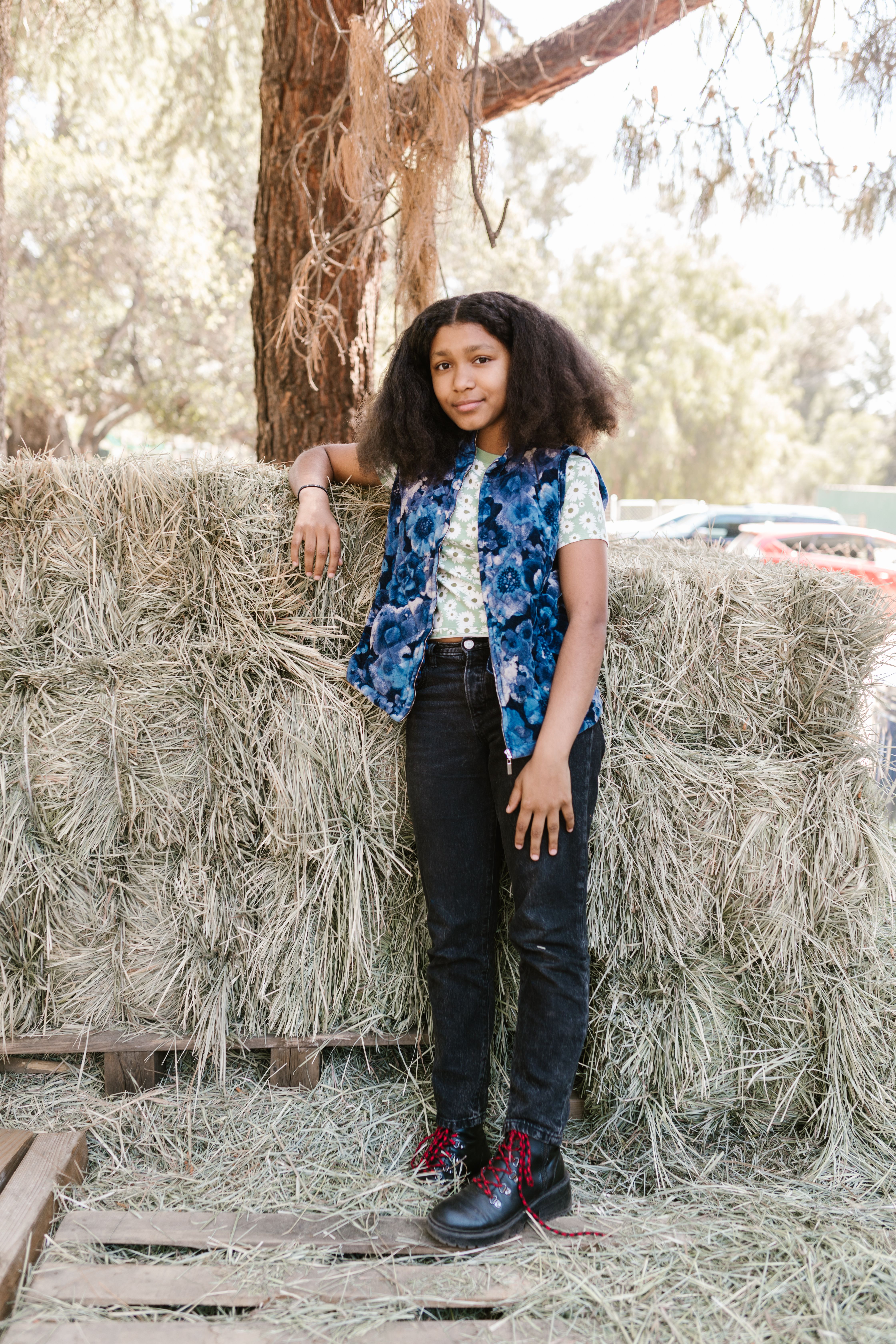 African American girl with afro hair leaning on a haystack in the countryside on a sunny day.