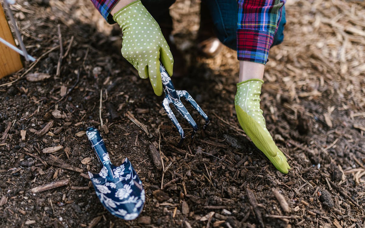 A person wearing gloves using garden tools in soil for planting.