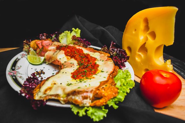 Delicious breaded cutlet topped with cheese and herbs, served with fresh salad, tomato, and lime wedge.