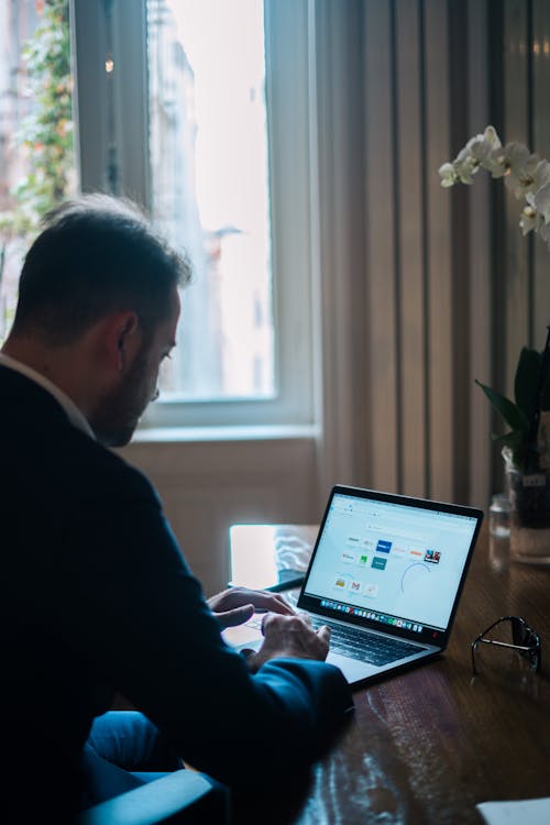 Concentrated businessman typing on laptop while working at table near window in daylight