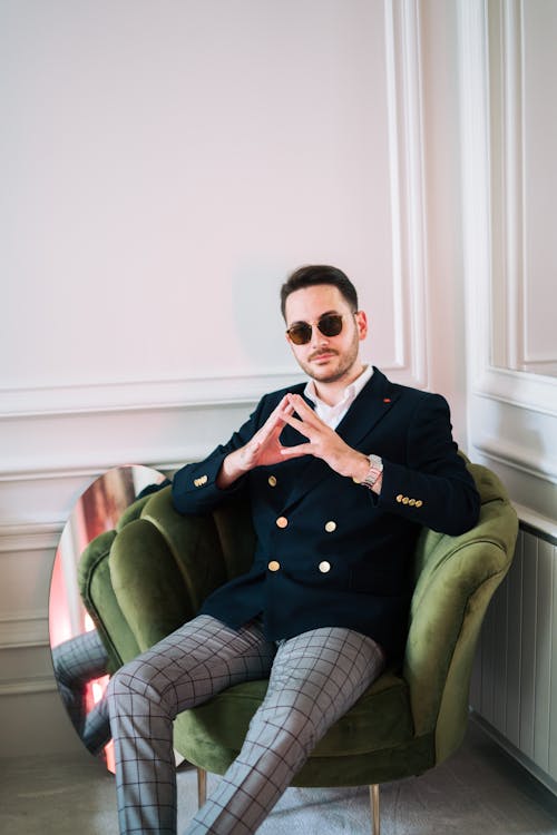 Free Confident man in sunglasses and classic jacket with trendy pants sitting in armchair in corner Stock Photo