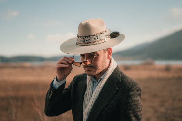 Man In Cowboy Hat Putting On Eyeglasses In Field