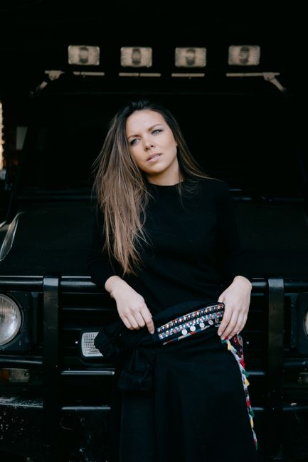 Fashionably dressed woman leaning on a black SUV, exuding style and elegance