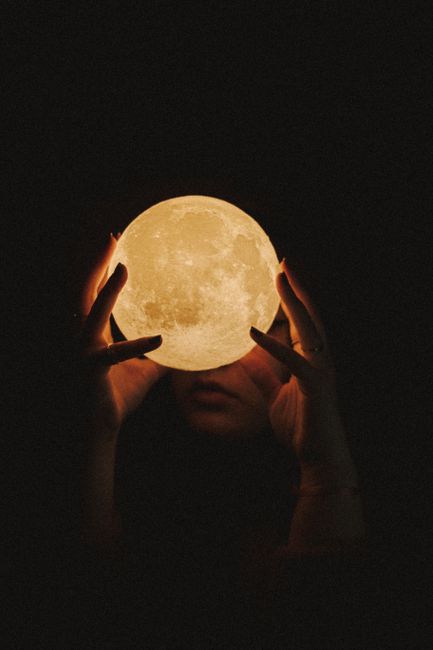 A person holds a glowing spherical object resembling the moon, creating a mystical and artistic scene.