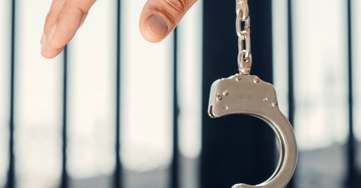 Photo by Kindel Media Hand grasping open handcuff with prison bars behind, symbolizing crime and justice.