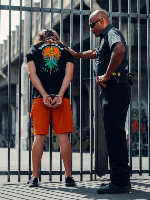 Free A Police Officer and a Man in Black Shirt Standing Near a Metal Fence Stock Photo