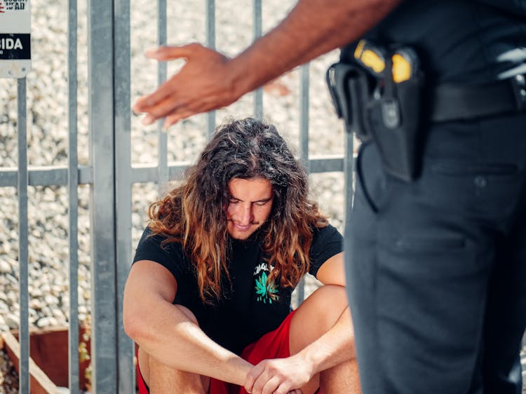 A Man In Black Shirt Sitting In Front Of A Policeman