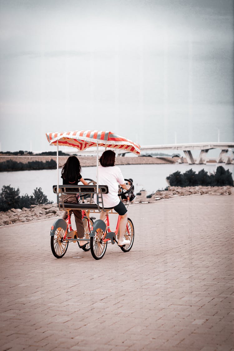 Two Women Cycling A Surrey Bike Near A River