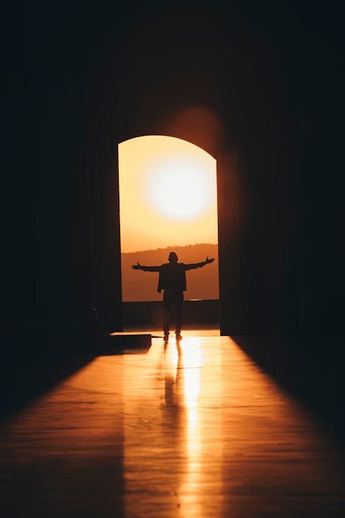 Silhouette of a Person Standing Near Entry During Sunset