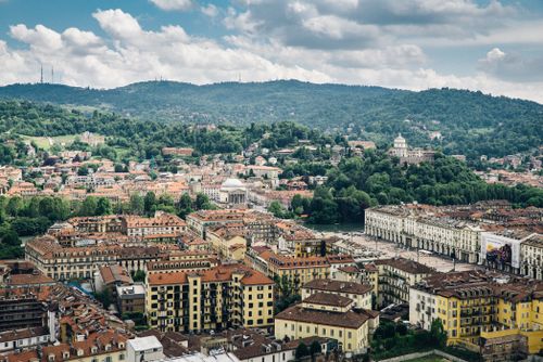 Free Aerial view of Turin cityscape featuring red-tiled roofs and lush green hills under a blue sky. Stock Photo