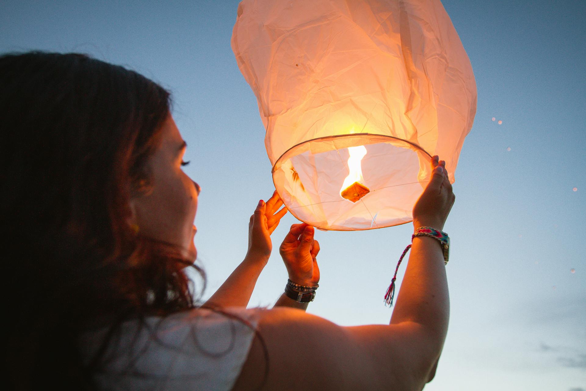 A woman releases a glowing paper lantern at dusk, symbolizing hope and celebration.