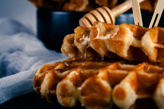 Close-up of warm waffles drizzled with honey, served on a black plate for a delicious breakfast treat.