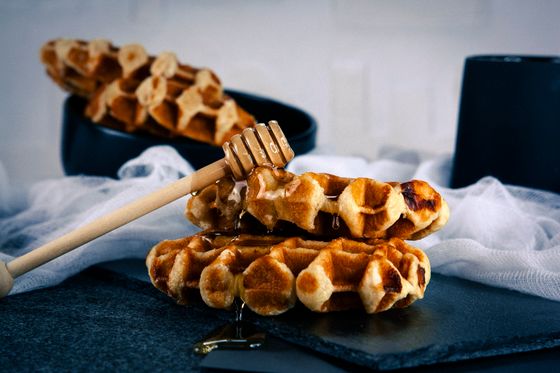 Stacked caramelized Liege waffles on dark slate with a honey dipper dripping honey