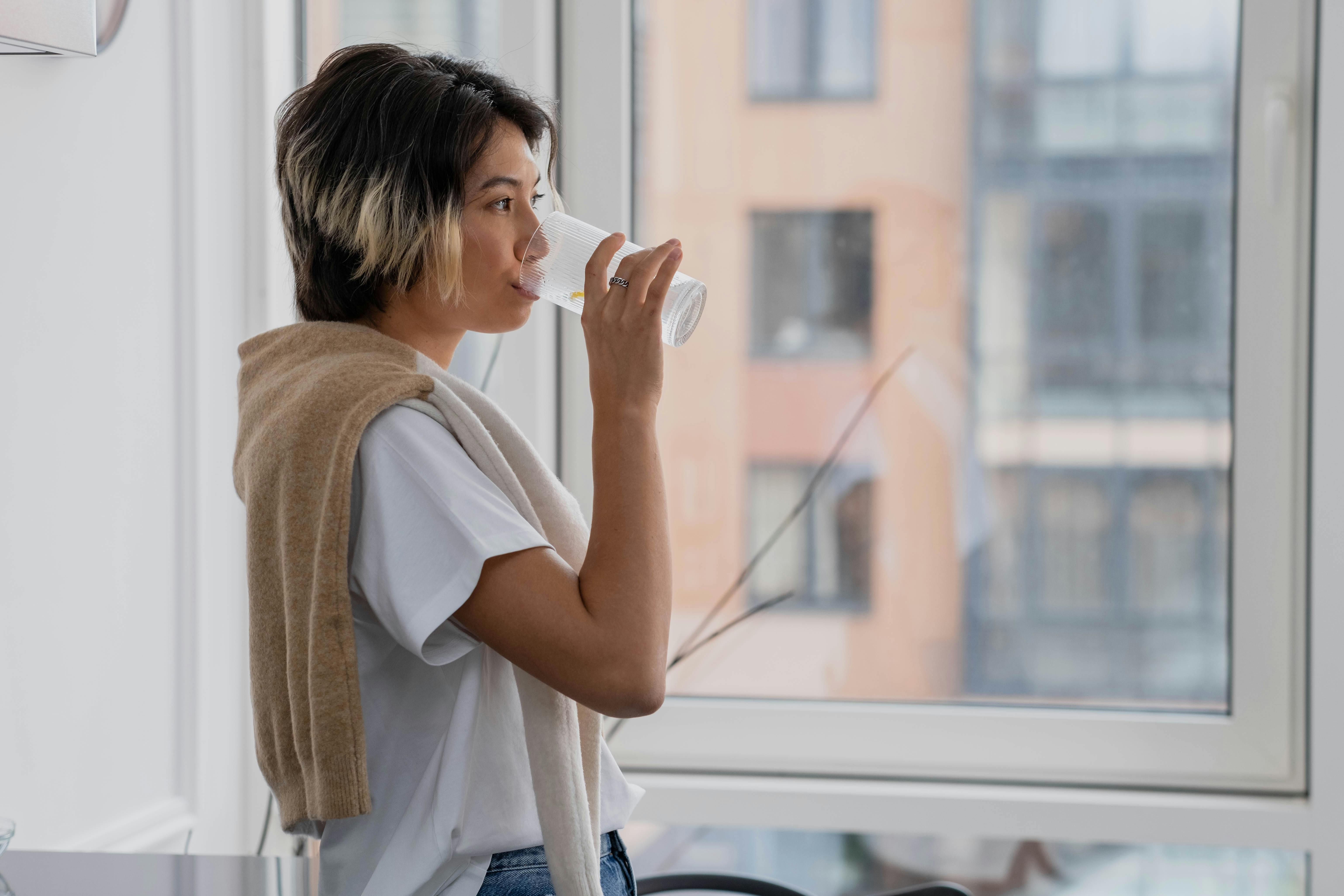 Woman Drinking Water near Glass Window · Free Stock Photo