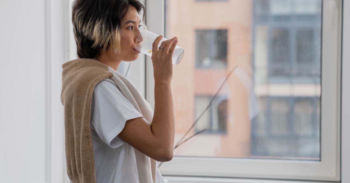 person drinking glass of water by window, coffee cup on counter in background