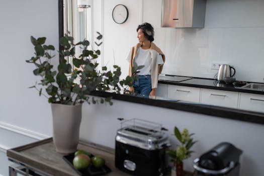 A woman looks out the window enjoying the morning light in a sleek, modern kitchen.