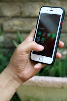 A person holding a smartphone with social media apps visible, set against a natural backdrop.