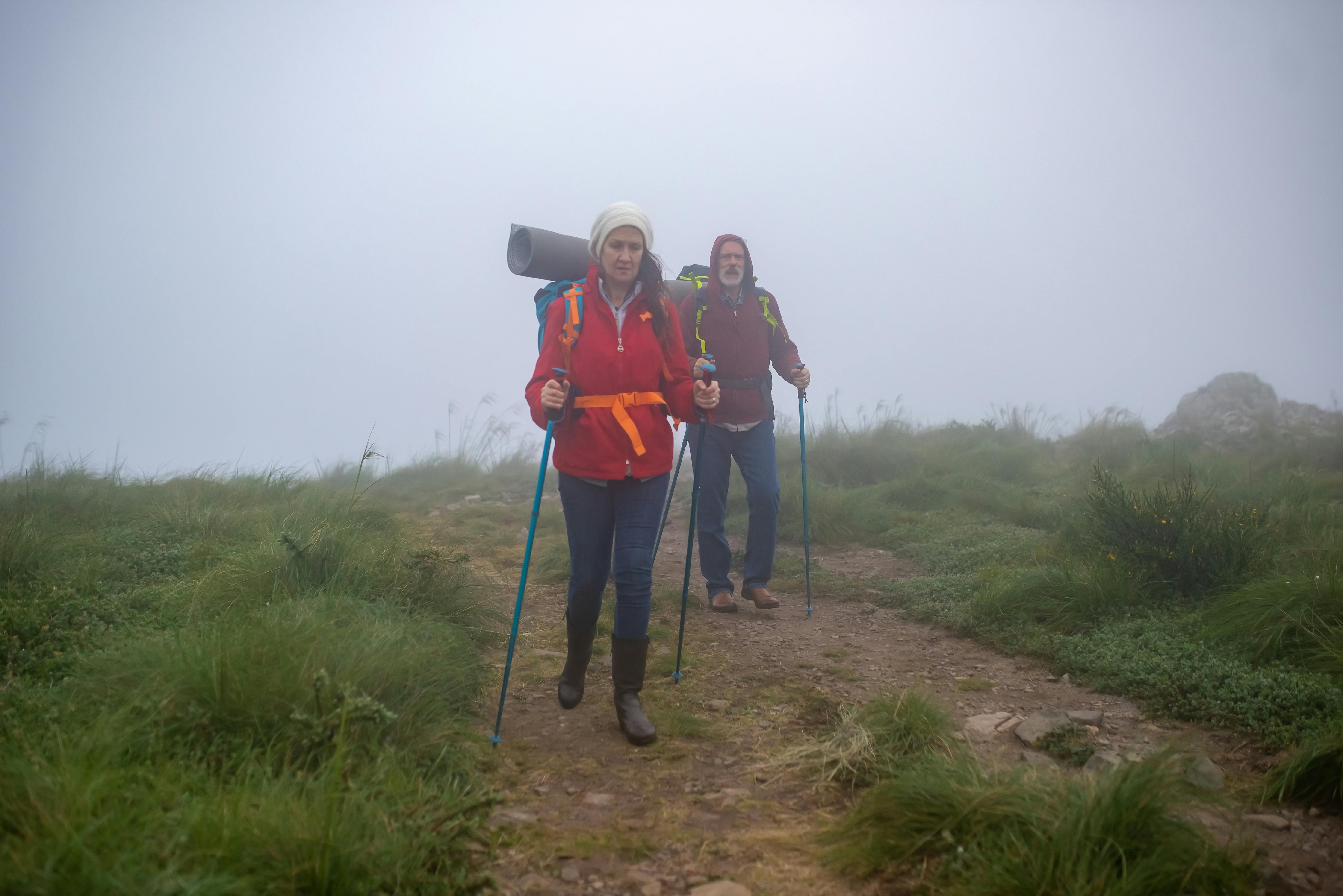 An elderly couple hiking with trekking poles on a foggy trail in Portugal.