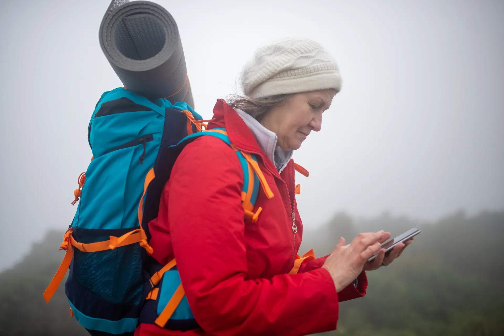 A hiker checking a phone on a foggy mountain trail A hiker checking a phone on a foggy mountain trail