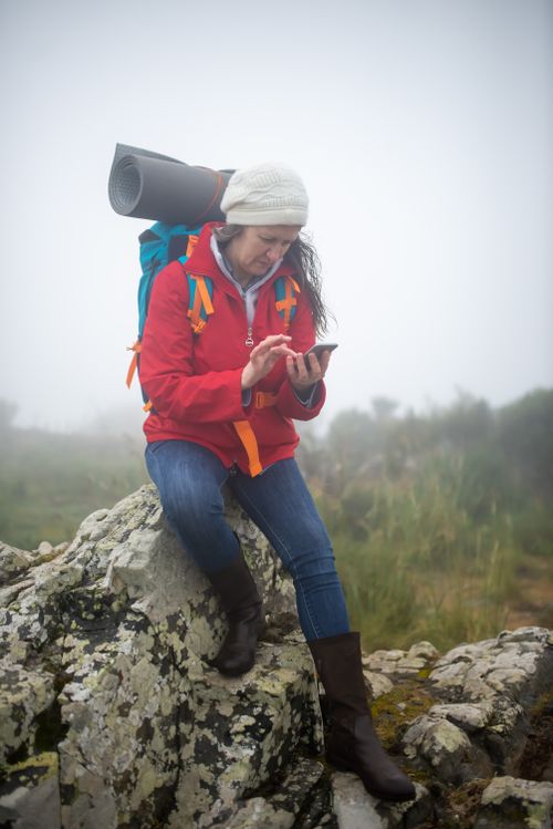 Free Woman hiker checking smartphone on a rocky terrain in foggy Portugal, blending technology with nature. Stock Photo