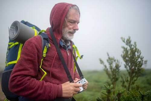 Man in Red Hoodie Wearing Blue and Yellow Backpack Holding White Camera