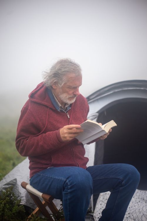 Free Senior man enjoying a peaceful morning reading outside a tent in the foggy Portugal wilderness. Stock Photo