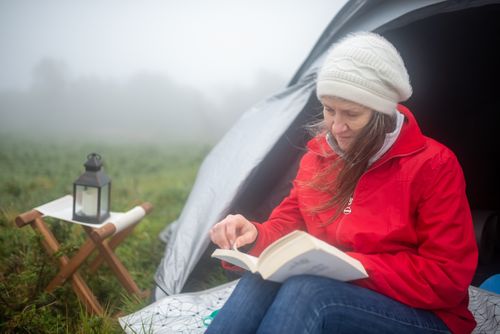 Free A woman enjoys reading outside her tent in a foggy meadow, embracing a tranquil camping experience. Stock Photo
