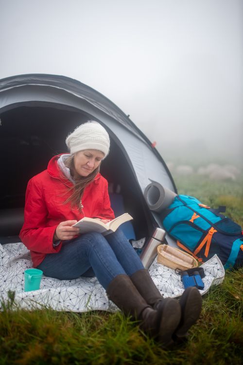 Free A woman enjoys reading a book outside her tent on a misty day in Portugal. Stock Photo