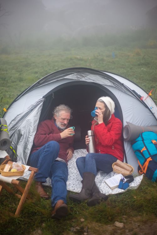 Free A senior couple enjoys a cozy camping experience in a misty hillside setting, sipping hot drinks. Stock Photo
