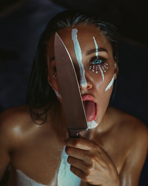 Young woman with artistic makeup licking kitchen knife