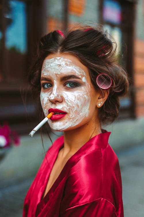 Coquette woman with hair curlers and face mask smoking cigarette