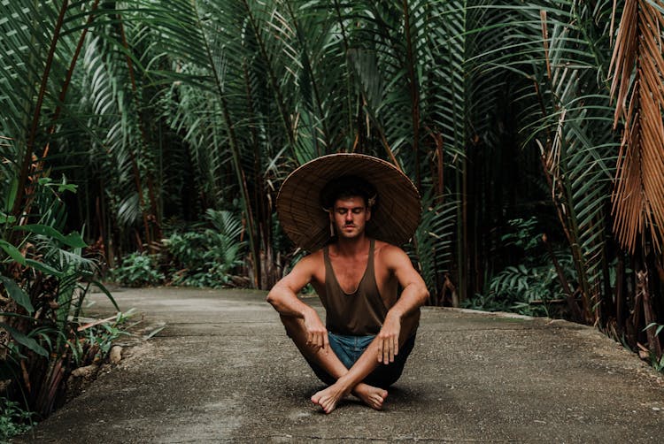 Positive Young Man Sitting In Lotus Position In Tropical Park