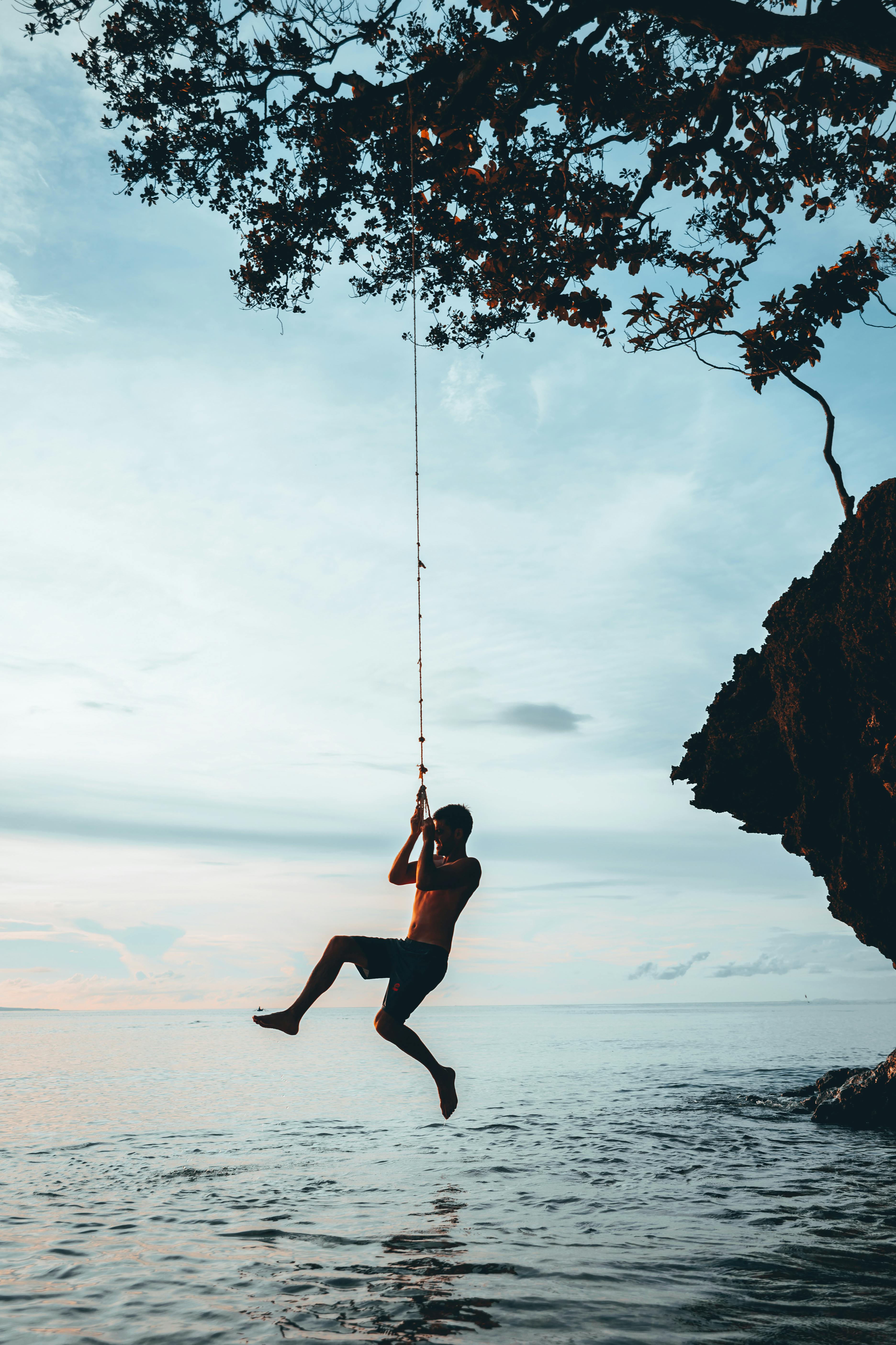 一个人的剪影在日落时从海洋上的绳索上快乐地摆动