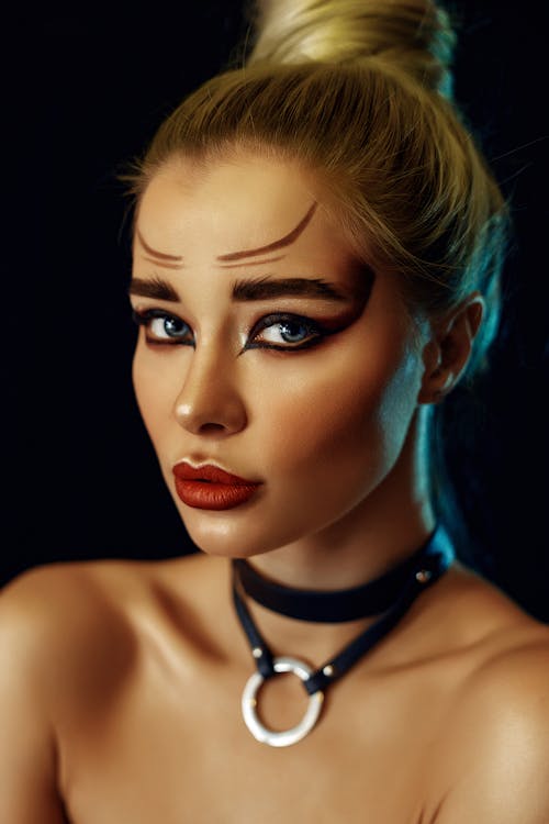 Free Young female model with bright creative makeup and red lips looking at camera against black background Stock Photo
