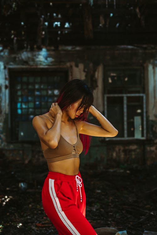 Young slim female in beige top and red sportive trousers standing near old destroyed building