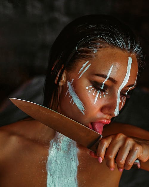 Young woman with artistic makeup licking knife