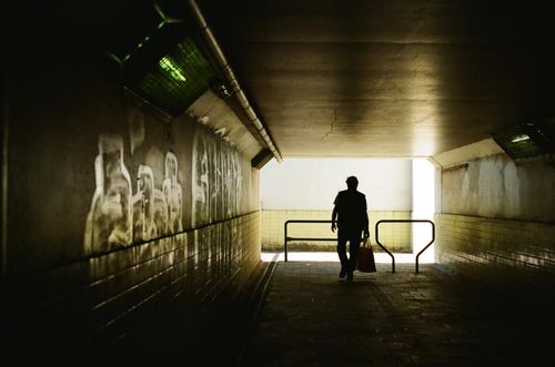 Free A solitary figure walks through a dark underground passage with graffiti, creating a striking urban silhouette. Stock Photo