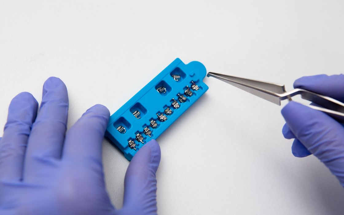 Hands of dentist in lilac latex medical gloves with dental tweezers and set of metal brace system