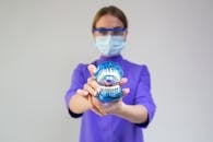 Female dentist in medical mask and protective eyeglasses demonstrating dental cleaning system with braces