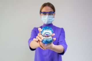 Female dentist in medical mask and protective eyeglasses demonstrating dental cleaning system with braces