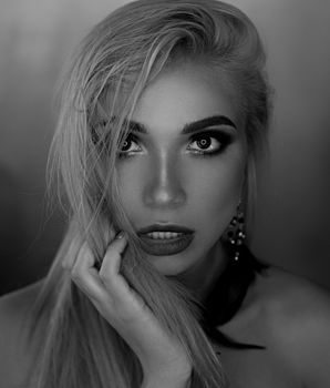 Black and white of young sensual female model with bright makeup touching hair with fingers and looking at camera