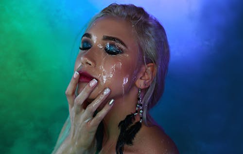 Alluring young female with closed eyes and glitter facial makeup touching face on gradient background
