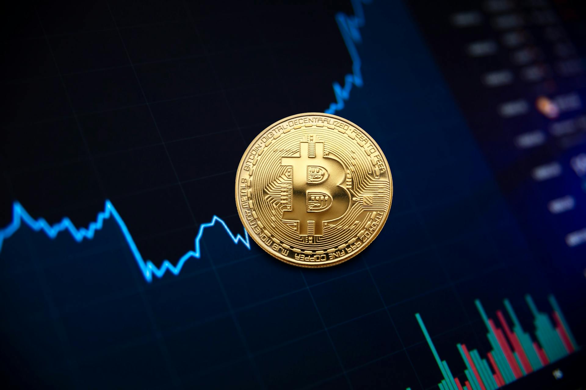 Golden bitcoin coin on background of chart showing indicators of changes in cryptocurrency rates