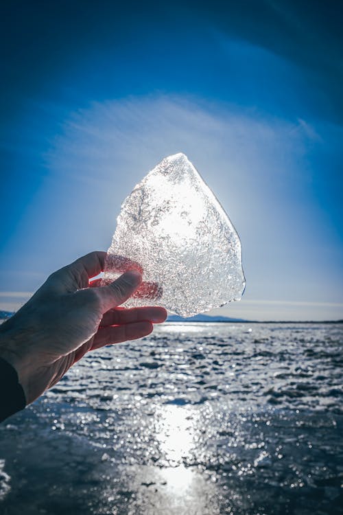 Person reaching out hand with ice against sunlight