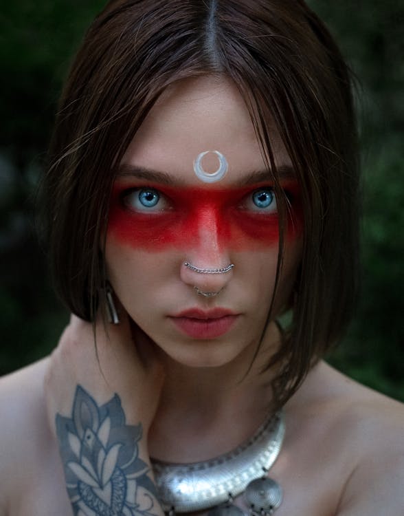 Charismatic female with bright blue eyes and creative makeup looking at camera against blurred dark background